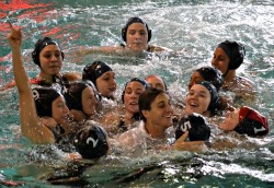 Members of the women's water polo team surround Coach JJ Addison in celebration moments after the team clinched its first league championship.