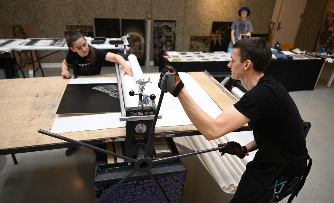 A student works with a guest at the woodcut printmaking workshop.