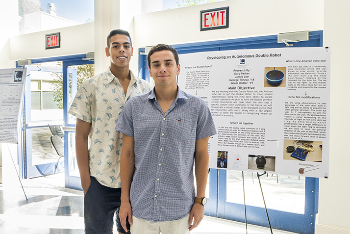 Jaleel Watler 19 and George Tilneac 18 pose in front of a poster about their work to develop an autonomous double robot. 