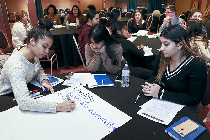 Three students write ideas on a poster board as part of an activity at the conference.