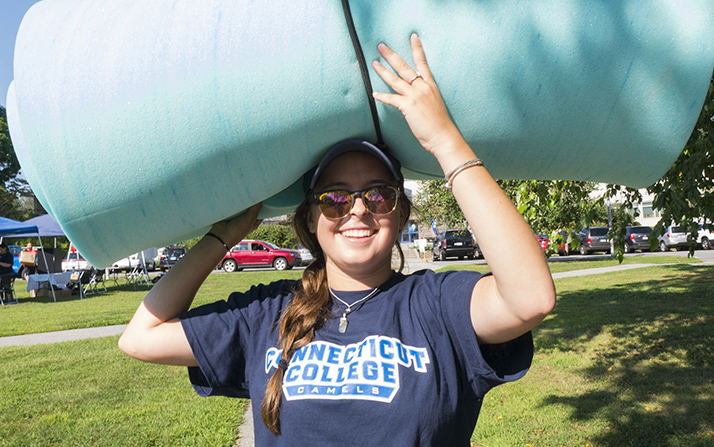 A young woman carries a mattress topper on her head. 