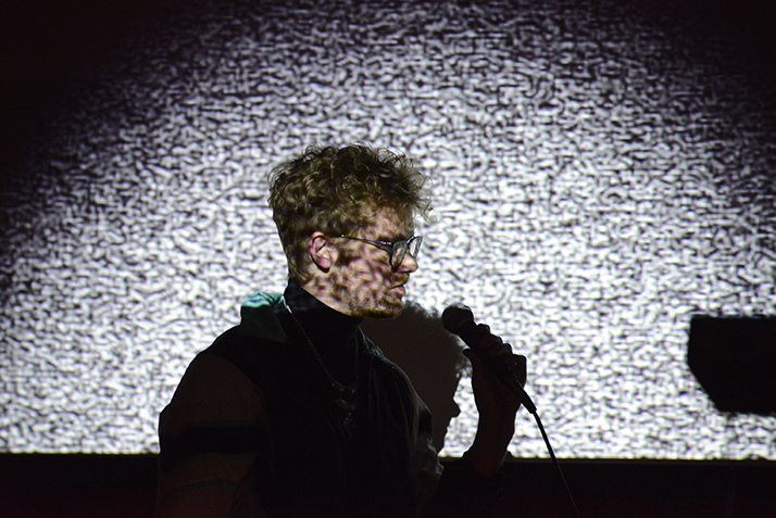An artist performs in front of a projection screen at the Ammerman Center Symposium