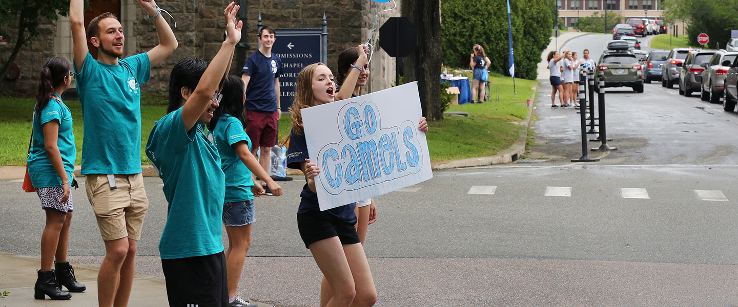 Upperclass students welcome first-years to campus with inviting signs at the college entrance.