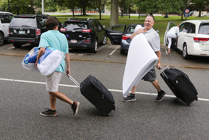A father carries a mattress topper while his son lugs a suitcase. 