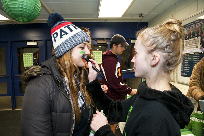 A student paints another student's face green before the start of the annual Green Dot Hockey Game.