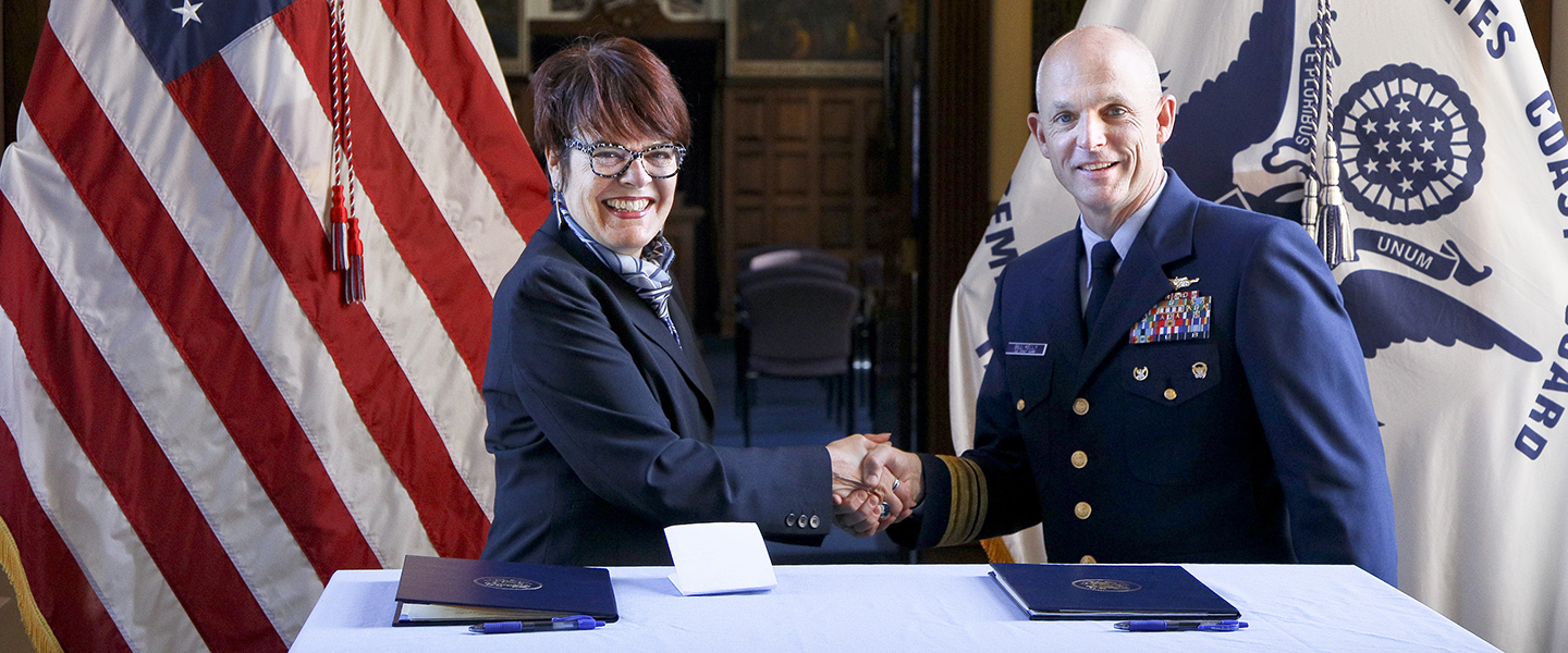 President Katherine Bergeron and the superintendent of the U.S. Coast Guard Academy, Rear Admiral William G. Kelly, shake hands. 