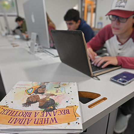 Students research various children's books in a college computer lab.