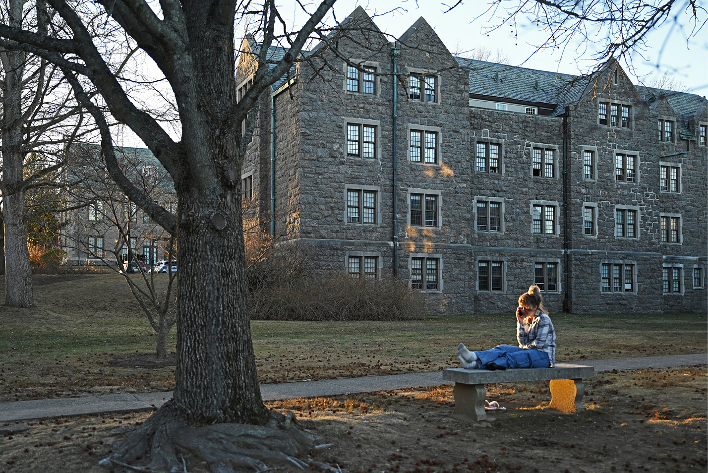 A student sits on a bench outside her dorm as the sun goes down.