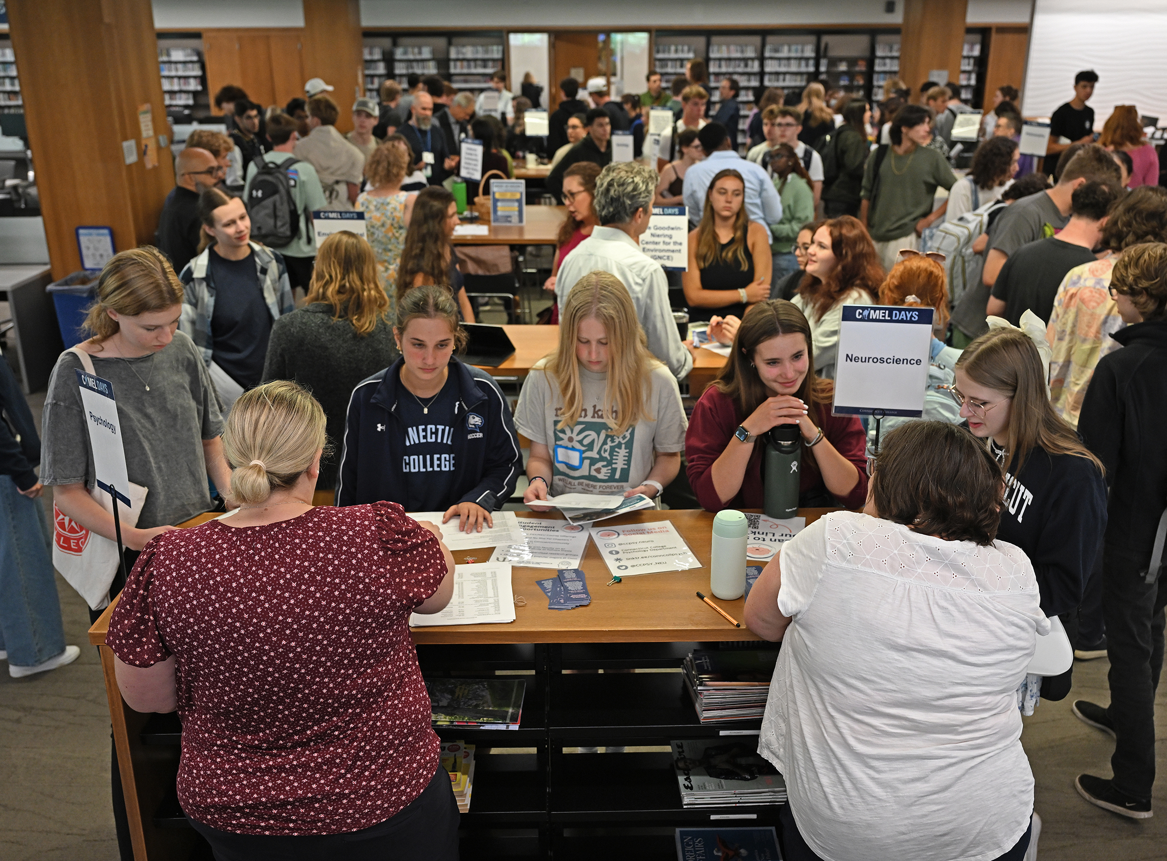 A crowd of students meet with faculty in a library.