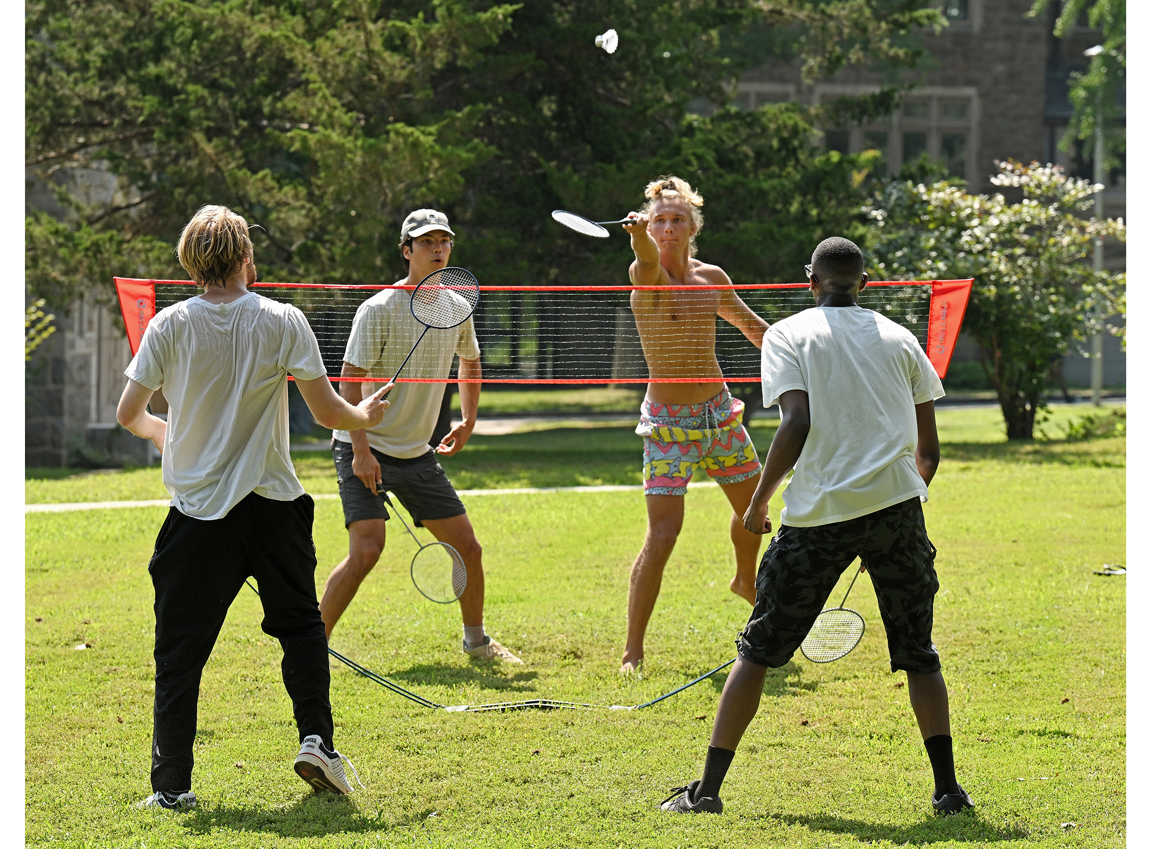 Students play badminton on a lawn.