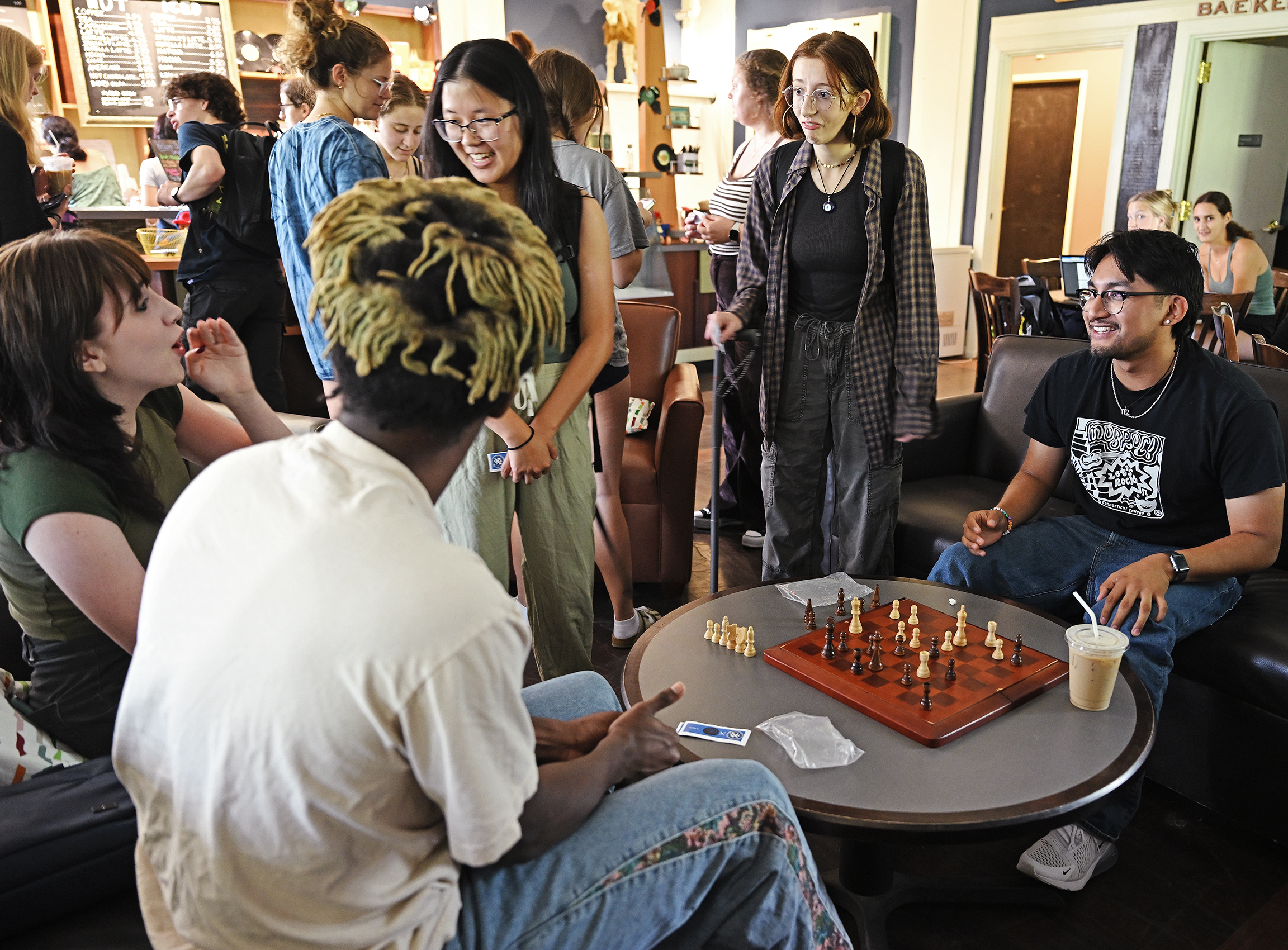 Students play chess around a low table in a coffee shop.