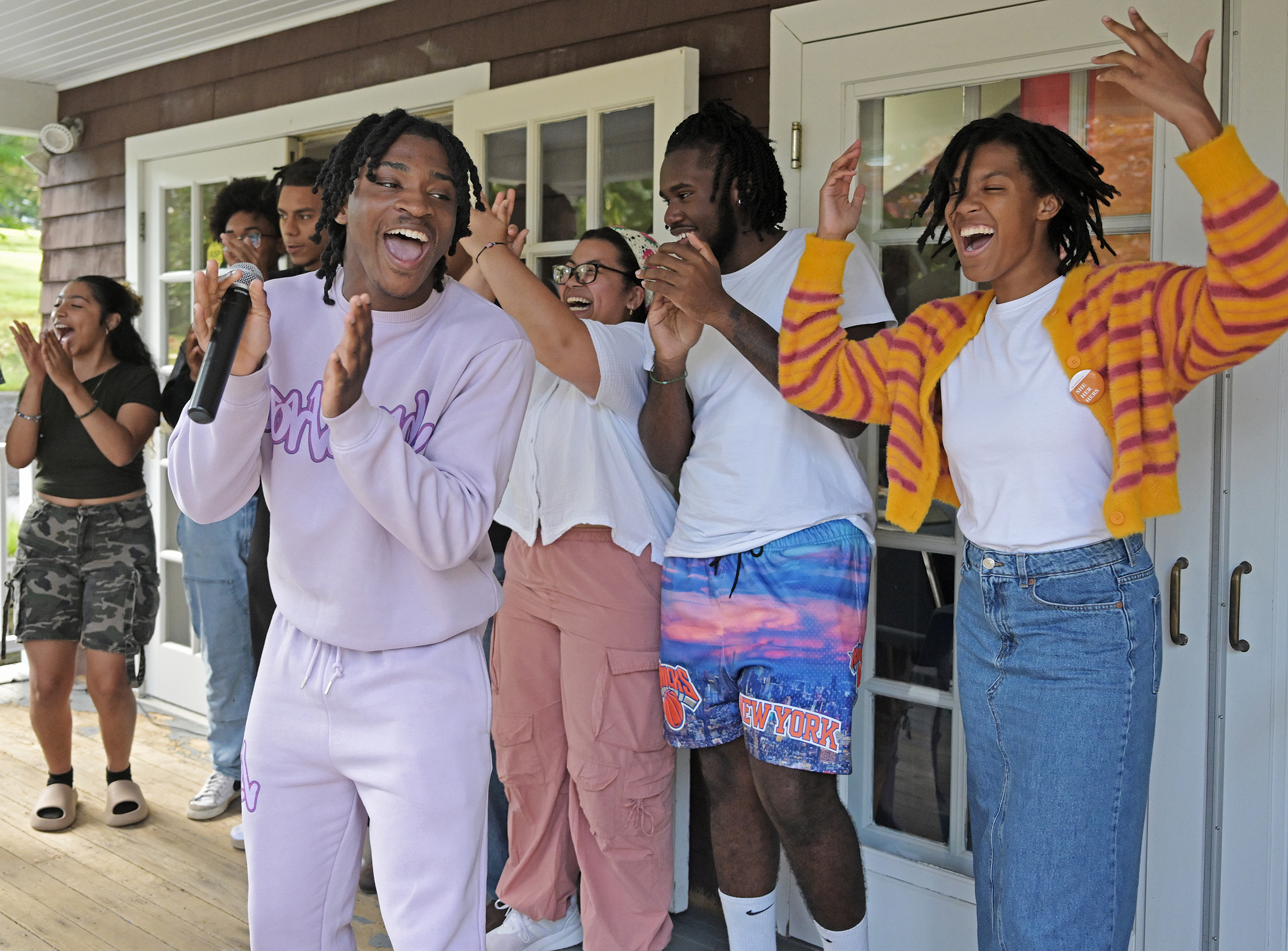 A group of students dance and gesture to a rap on a covered porch.