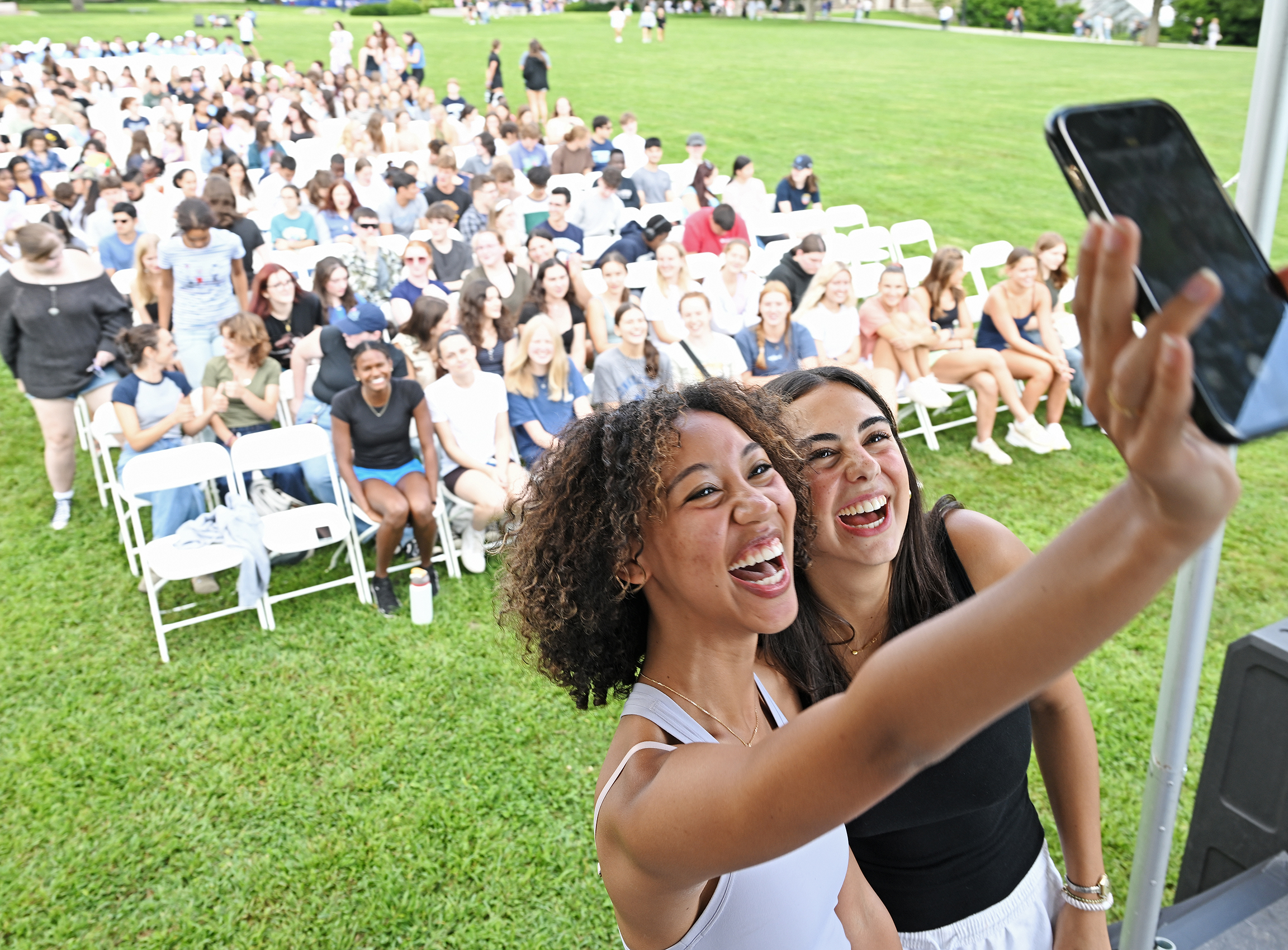 Two students take a selfie photo together in front of their classmates.