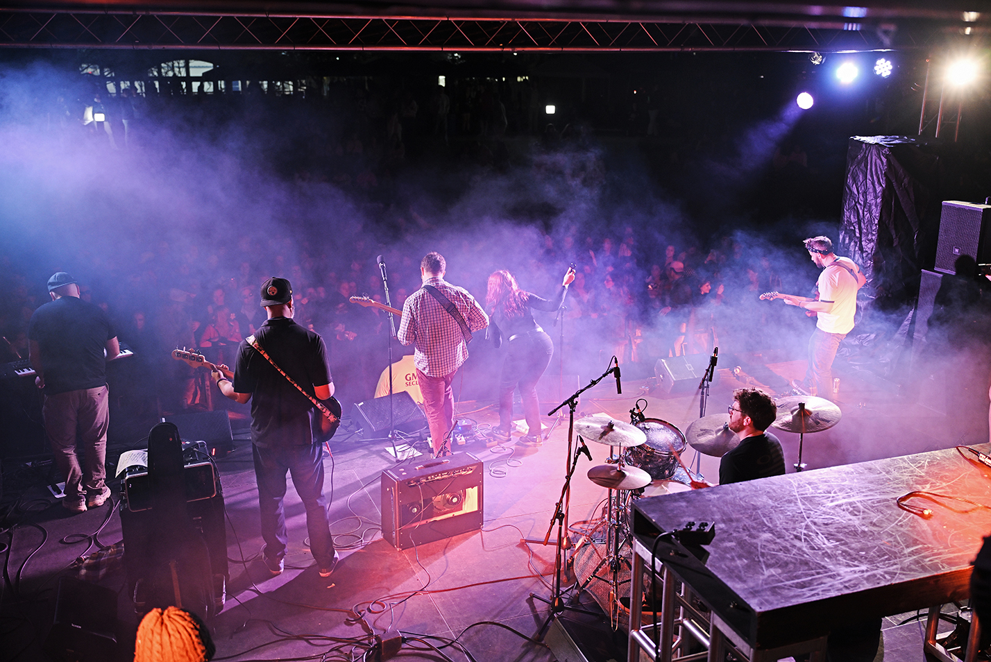 A band performs on stage as seen from behind with fog shrouding the audience.