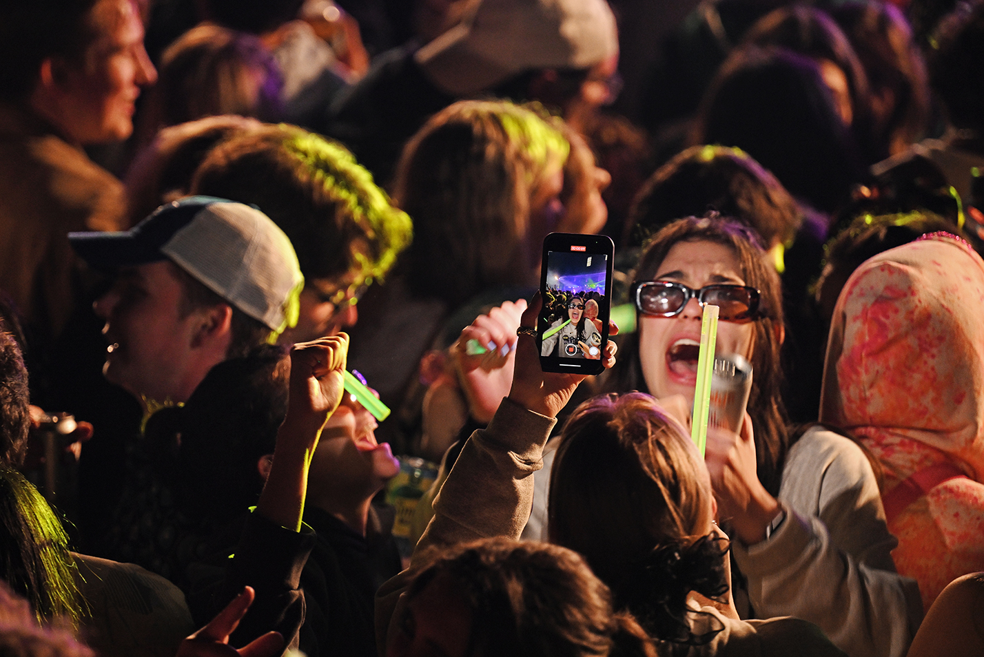 A student makes a face for a smartphone camera while amidst a crowd at a concert
