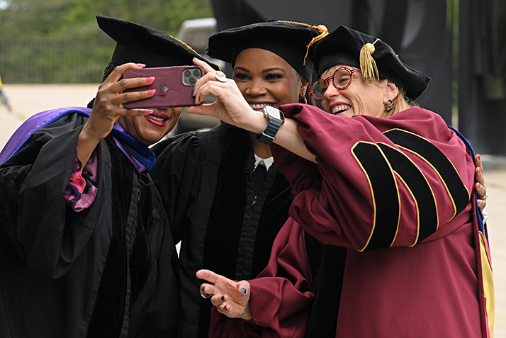Three women in academic regalia take a selfie photo together
