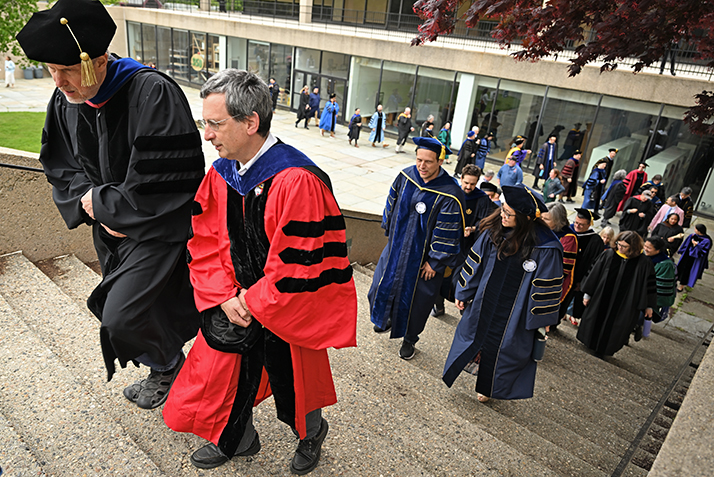 Faculty in their academic regalia process up stairs on their way to commencement exercises