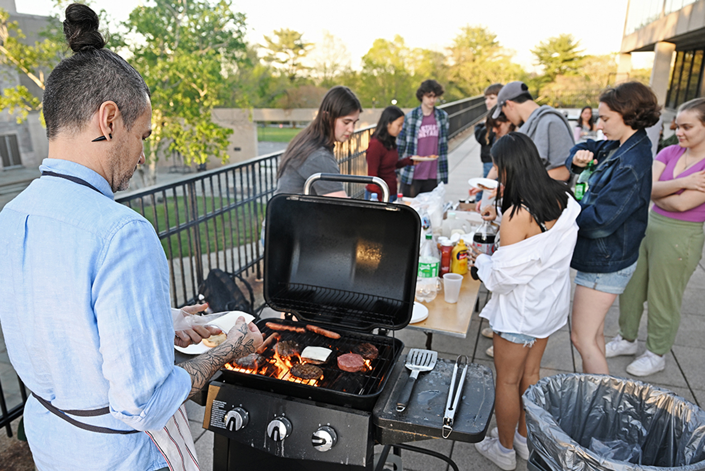 A professor grills food for graduating students at an outdoor gathering