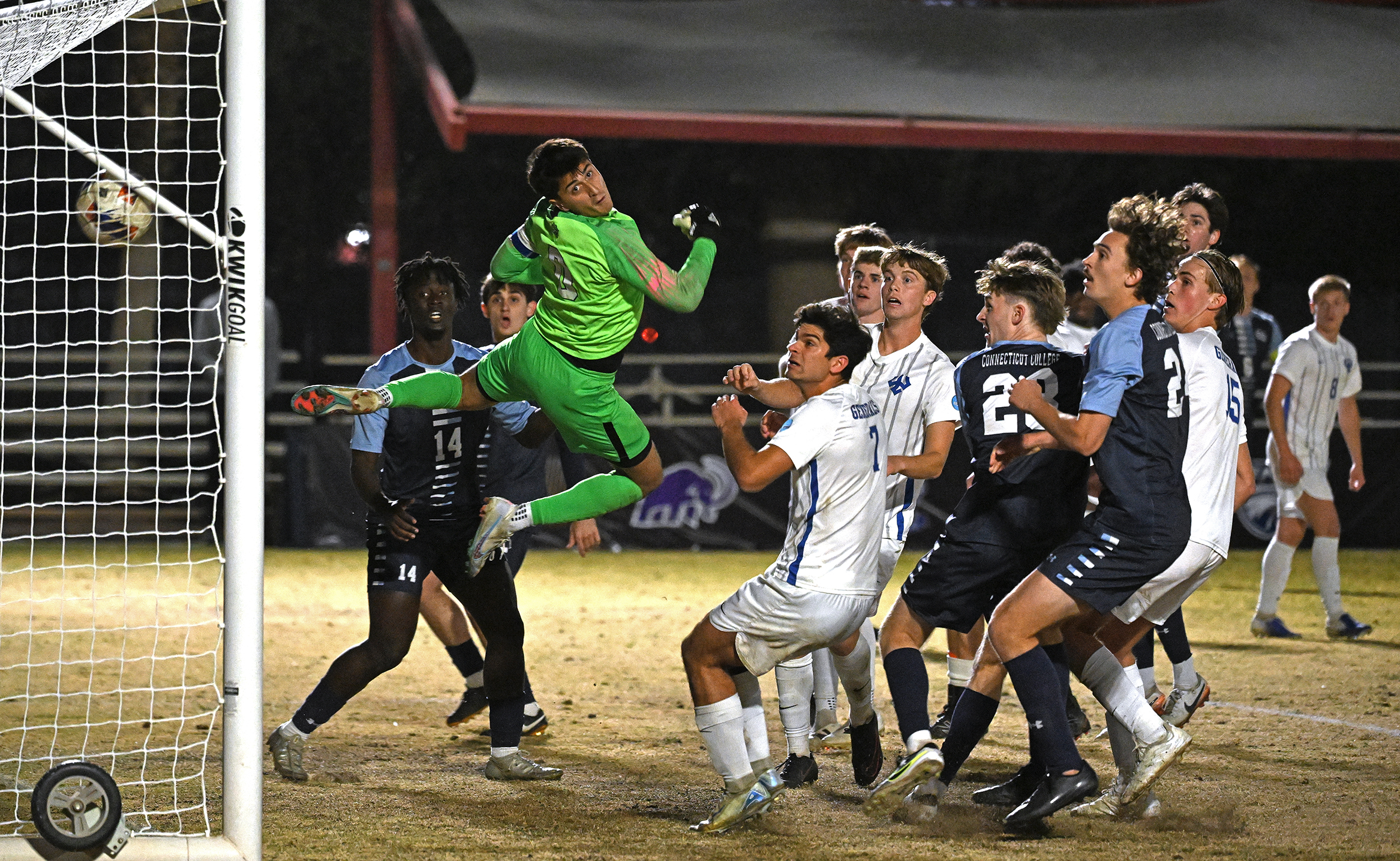 Soccer players watch as the ball goes into the goal.