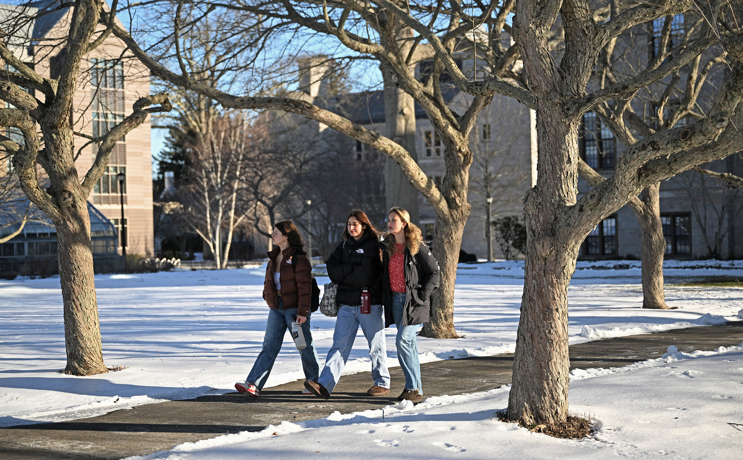 Three female students walking across campus in the snow.