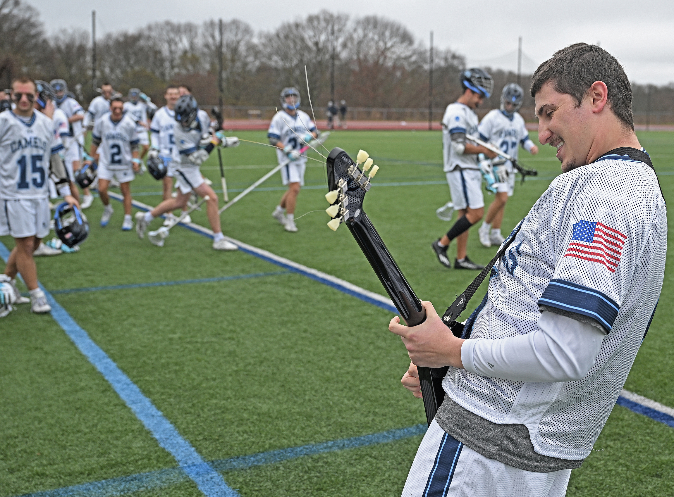 A lacrosse player performs the national anthem on an electric guitar before a game