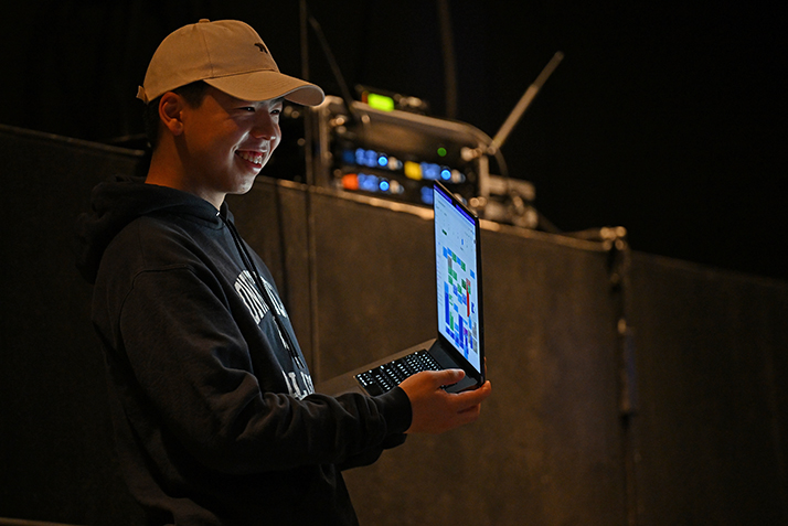 A student sound technician smiles while adjusting audio setting on a laptop computer