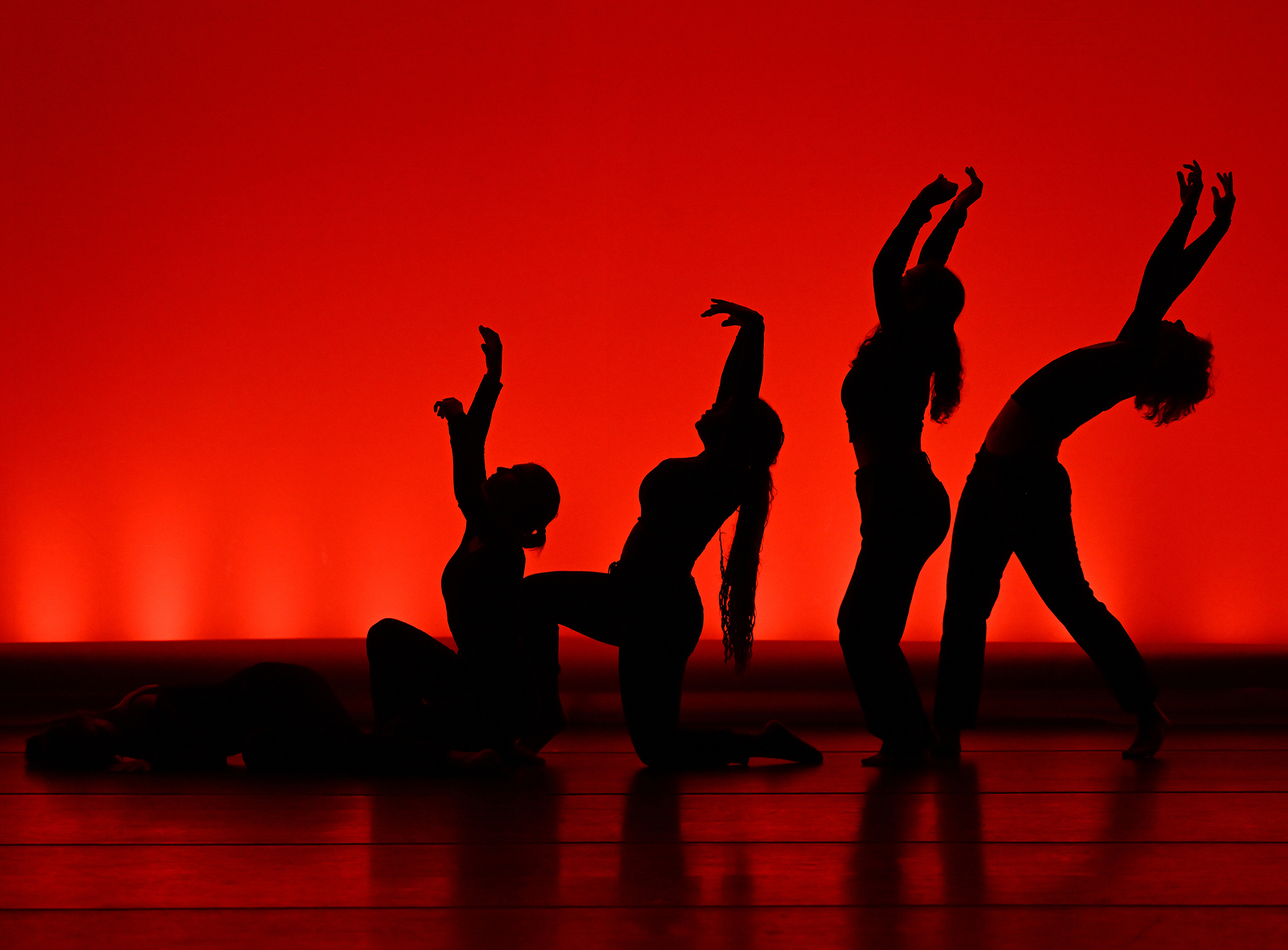 Dancers silhouetted against a rad background strike a pose on stage.