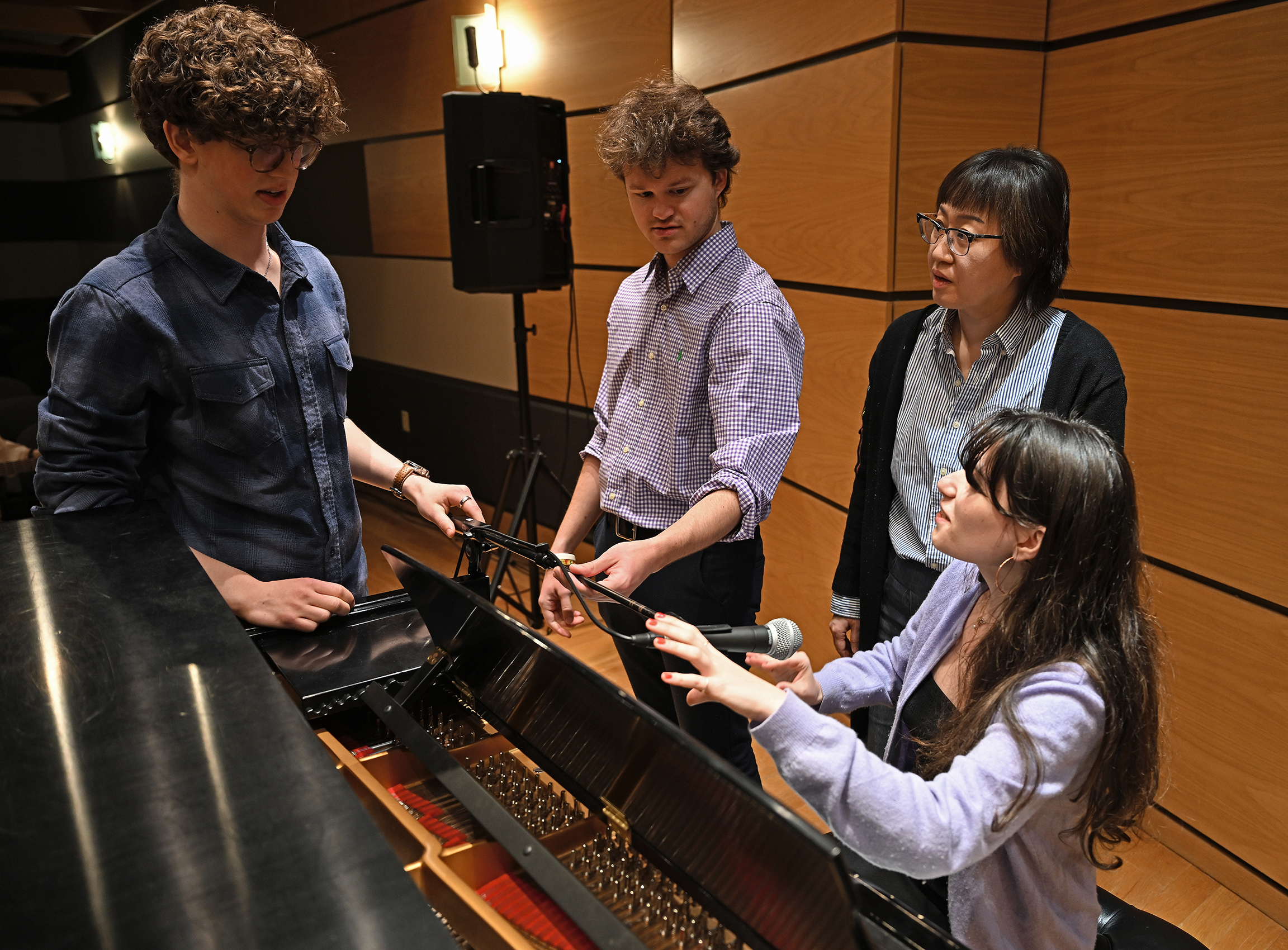 Musicians help one seated at the piano set up a microphone