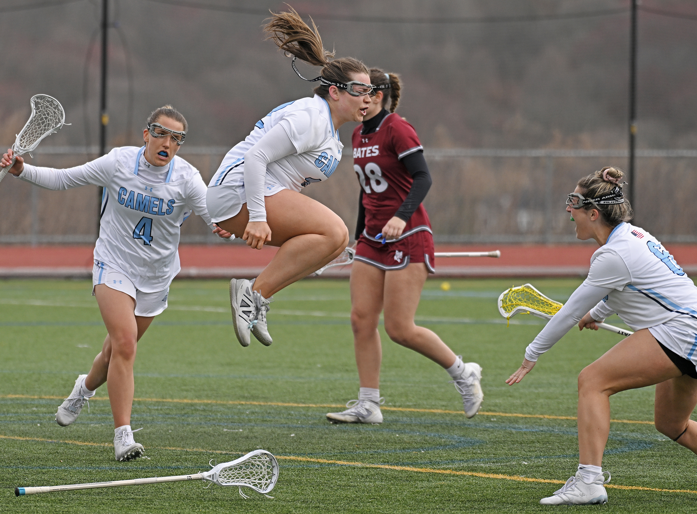 a women's lacrosse player jumps in the air to celebrate a goal with teamates