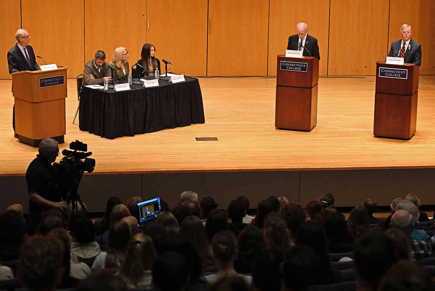 Candidates for U.S. Congress meet in a debate on stage in front of a panel and moderator.