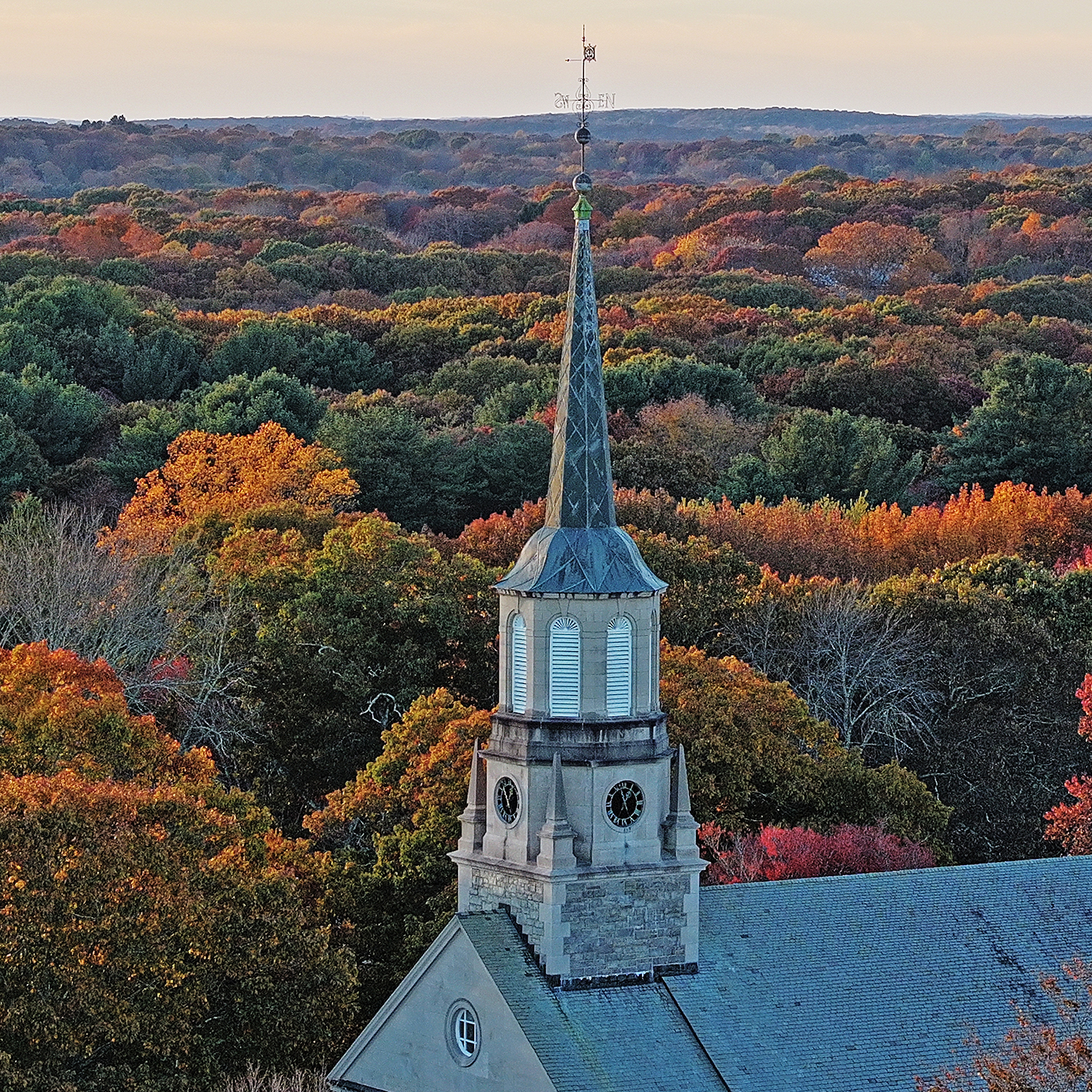 A chapel steeple stands out in front of a panorama of fall foliage color.