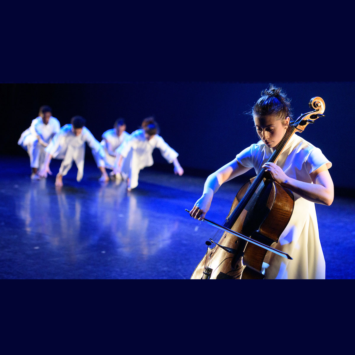 dancers approach a woman playing a cello